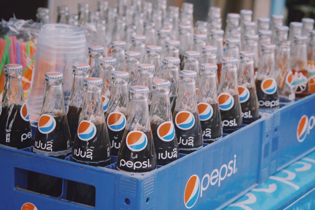 services-img A close-up of glass Pepsi bottles arranged in a blue plastic crate, showcasing a vibrant beverage display.