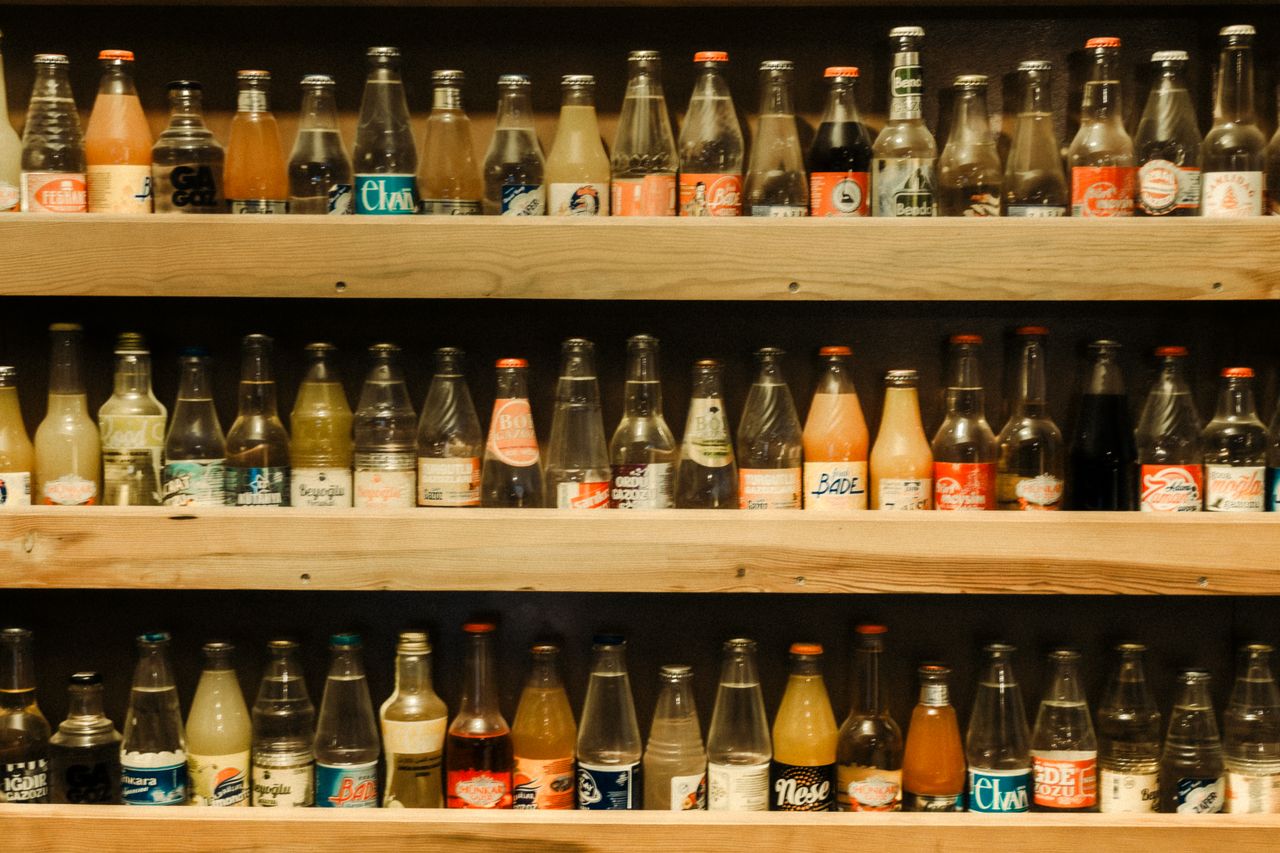 A collection of vintage soda bottles arranged on wooden shelves, showcasing retro designs.