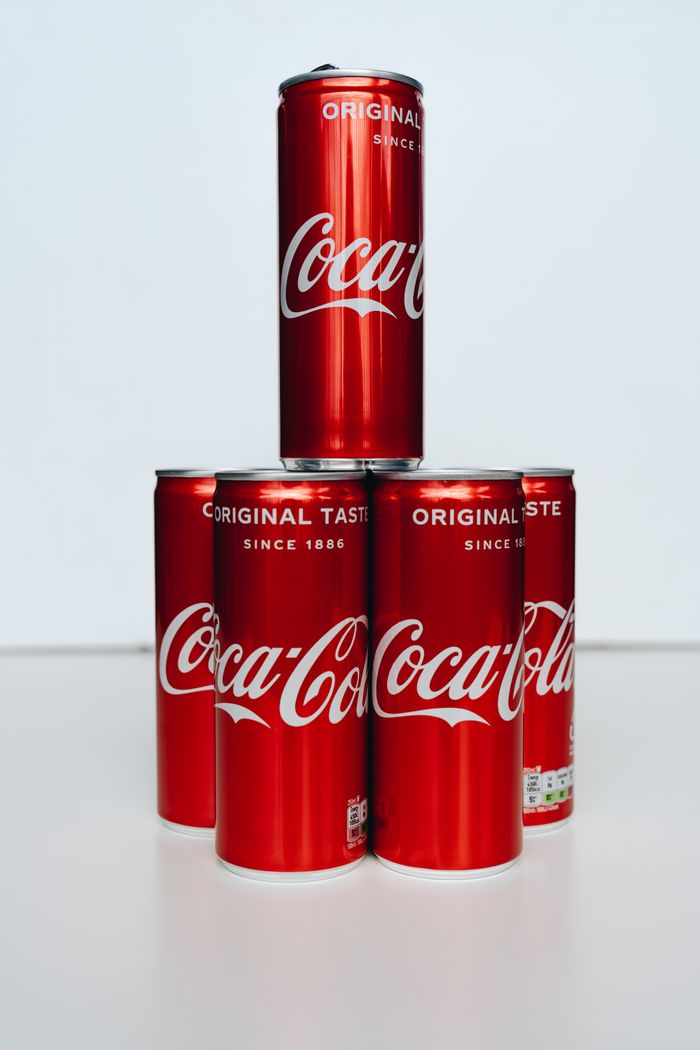 Set of Coca-Cola cans arranged in a pyramid on a clean white surface.