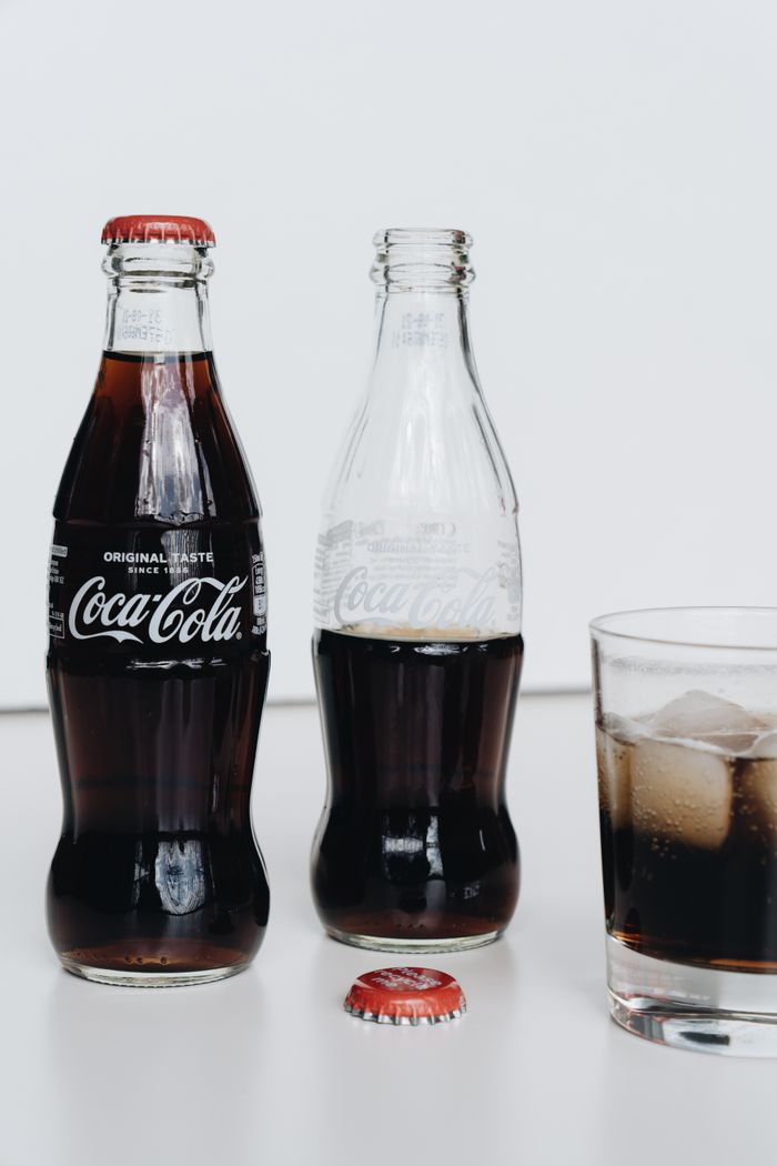 Classic Coca-Cola bottles with a refreshing iced drink on a minimalistic background.