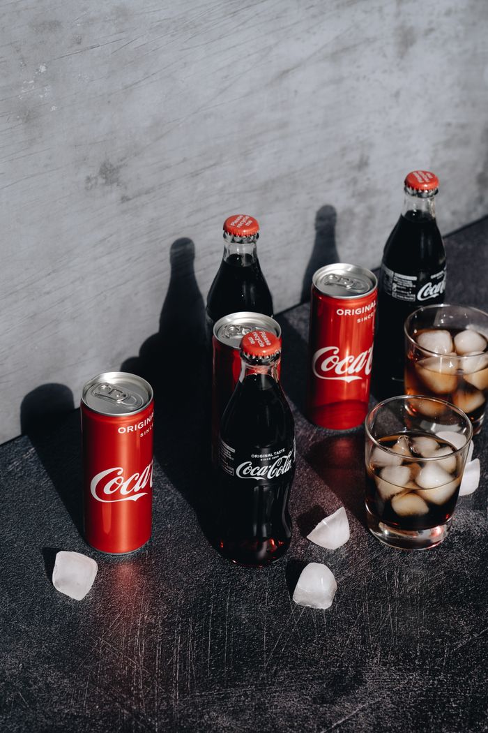 Chilled Coca-Cola in bottles and cans with ice cubes in glasses on a dark surface.