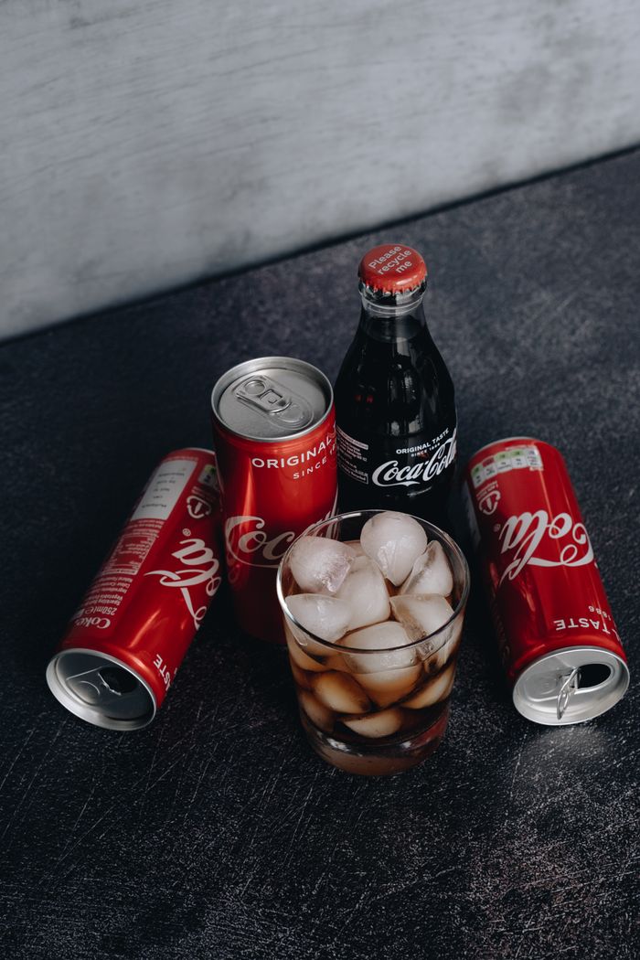 Chilled Coca-Cola in cans and bottles with a glass of ice; refreshing beverage setup.