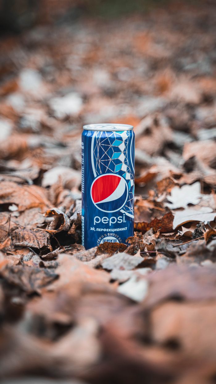 ours-journey Close-up of a Pepsi can surrounded by dried autumn leaves, emphasizing fall ambiance.